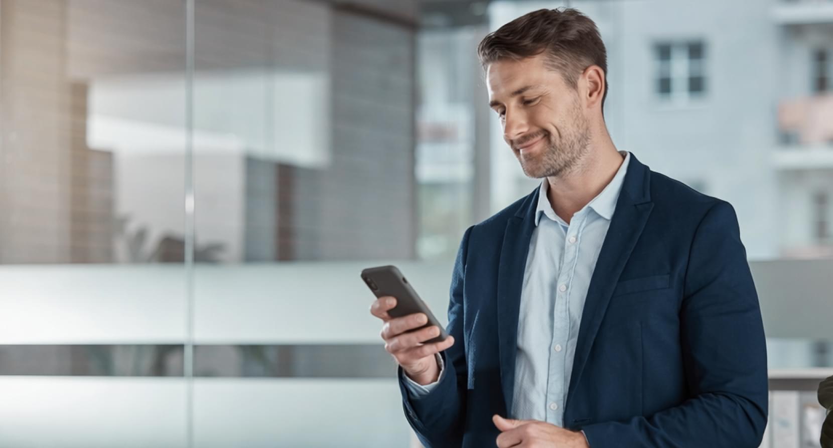 A business professional in an office checks his smartphone during a digital onboarding process.